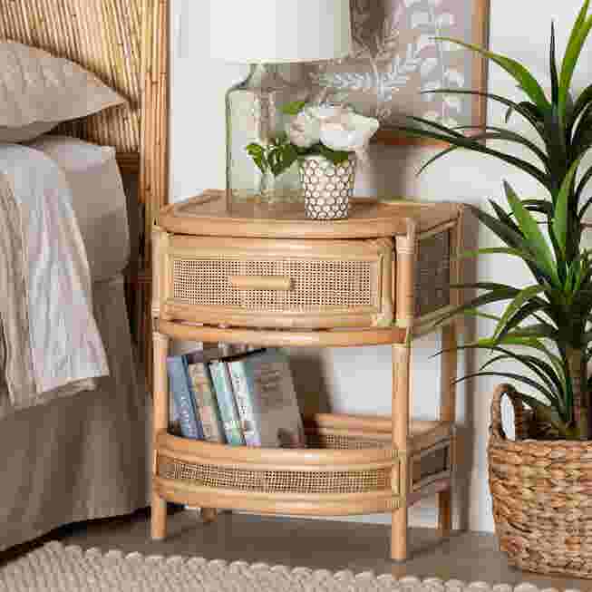 Rattan nightstand with a drawer and shelf, next to a bed and a plant.